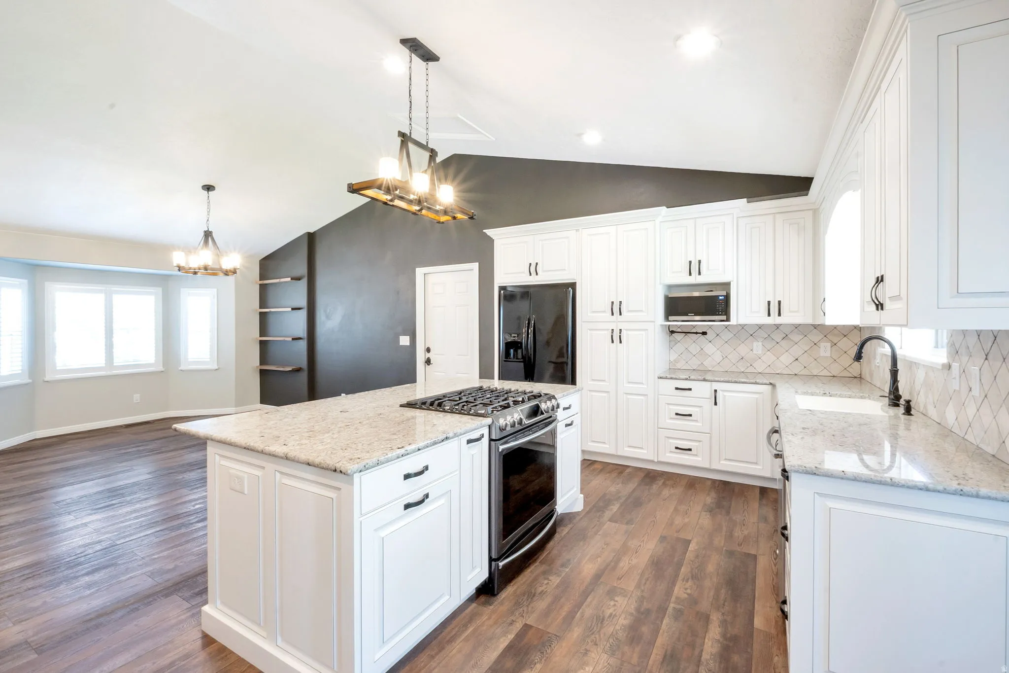 Modern kitchen featuring an island with built-in gas range, white cabinetry with dark hardware, stone countertops, and wood-finish flooring