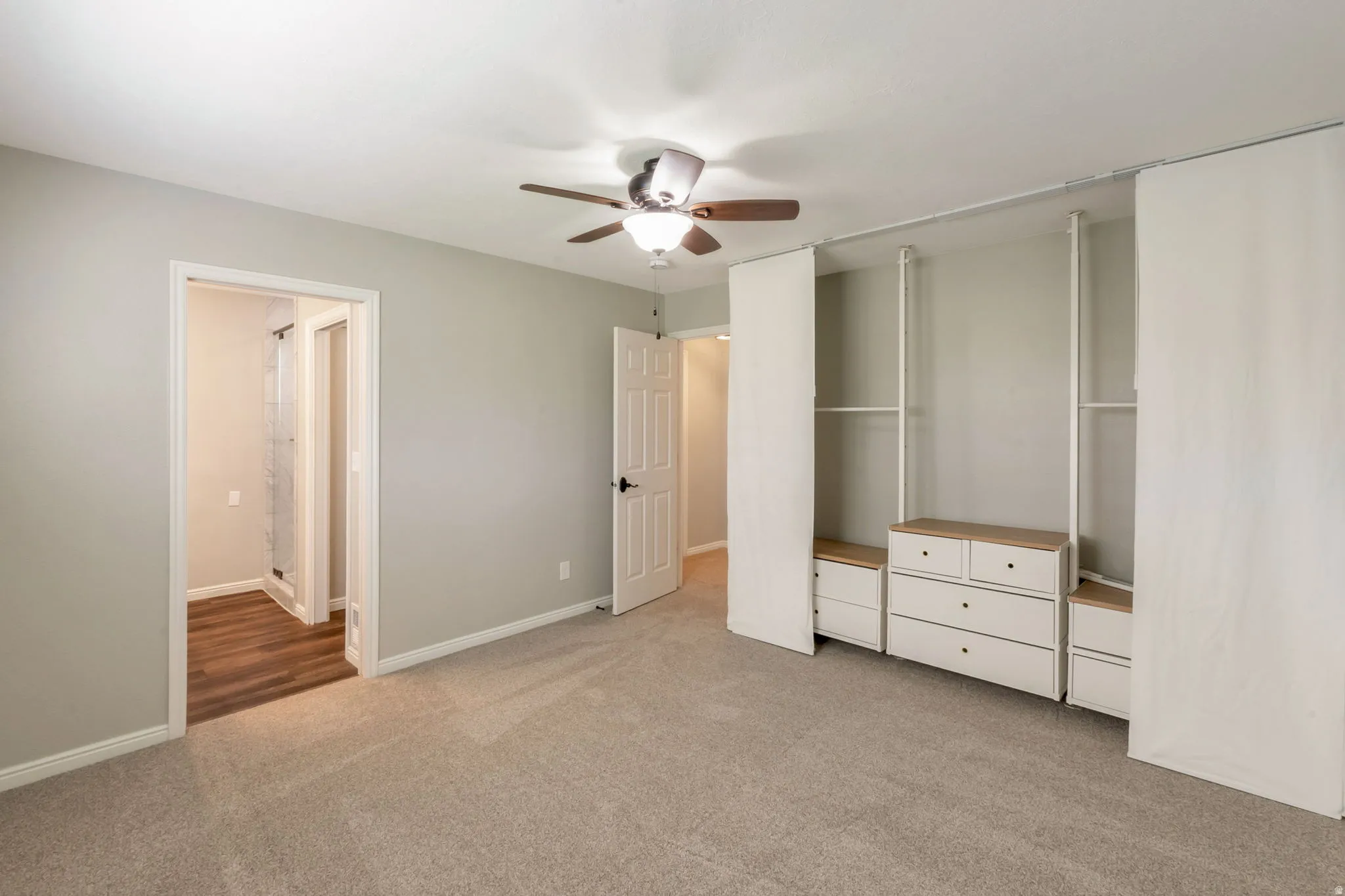 Carpeted bedroom featuring a ceiling fan with integrated lighting, light gray wall paint, white baseboards, and a built-in wardrobe system with drawers and shelving