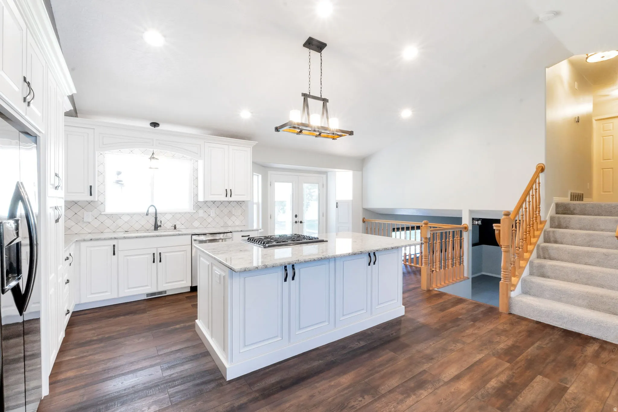 Spacious kitchen featuring white cabinetry, a large center island with a built-in cooktop, and granite countertops
