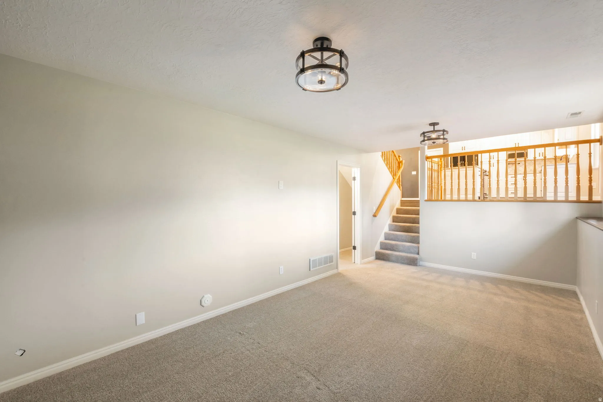 Carpeted lower-level living area featuring two flush-mount lighting fixtures with decorative metal and glass shades, light-toned walls, and white trim
