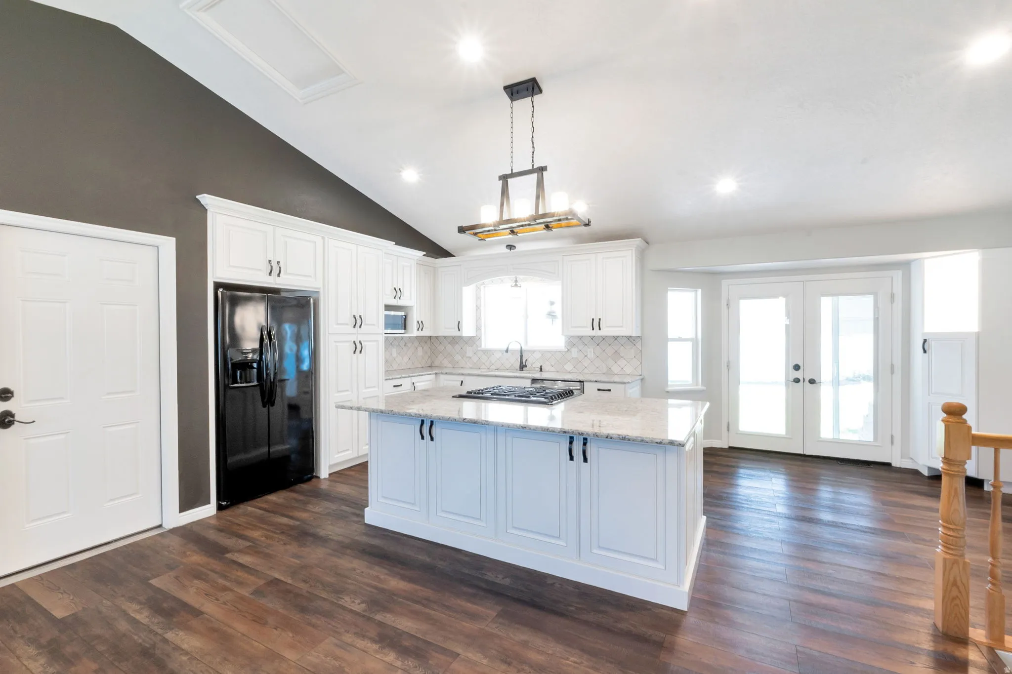 Bright kitchen featuring a central island with a gas cooktop, white cabinetry, and granite countertops