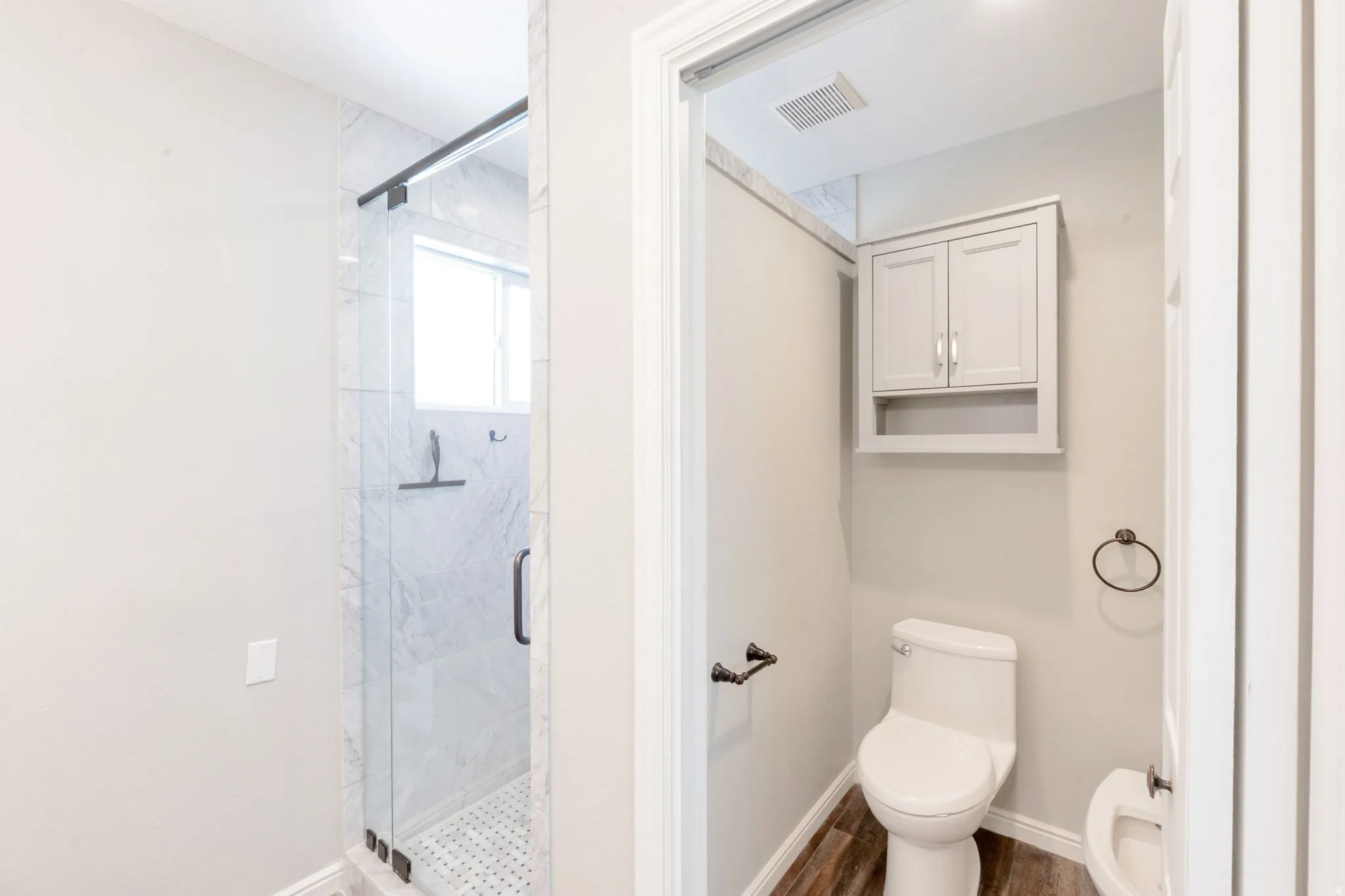Tiled shower with glass enclosure, window, and dark bronze fixtures