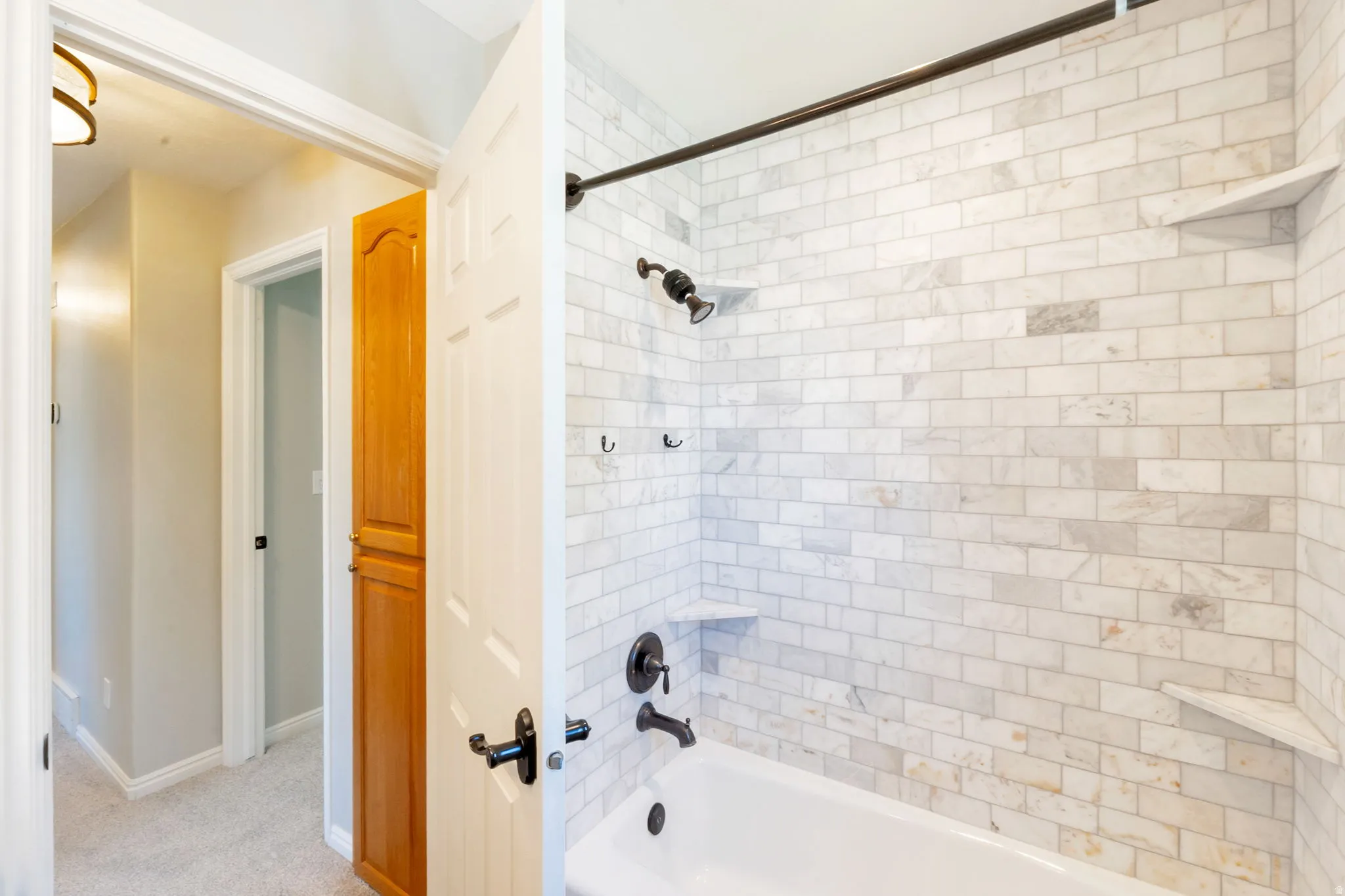 Bathtub and shower combination featuring white subway tile surround, dark bronze fixtures, and built-in corner shelving