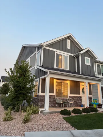 Two-story residence featuring a covered front porch with stone accents, board and batten siding, and a well-maintained lawn with decorative gravel landscaping