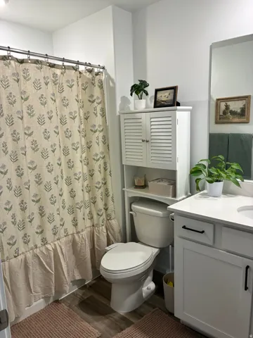 Bathroom featuring a white vanity with a quartz-finish countertop, wood-finish flooring, and a built-in over-toilet storage unit
