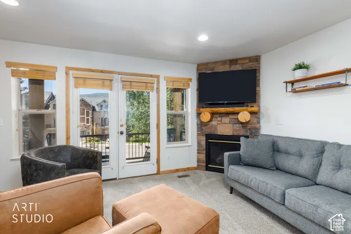 Living area featuring a floor-to-ceiling stone fireplace with a wood mantel, recessed lighting, double French doors, and an outdoor balcony