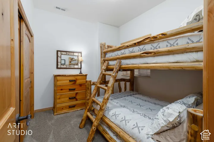 Carpeted room featuring natural wood-finish door, closet with bi-fold doors, and a wood-finish dresser with metal hardware