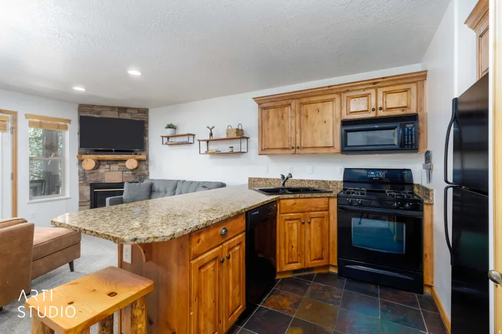 Kitchen featuring wood cabinetry, granite countertops, and black appliances, including a built-in microwave, gas range, and refrigerator