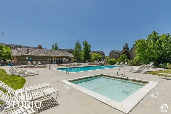 Community swimming pool and hot tub with surrounding concrete patio and abundant lounge seating