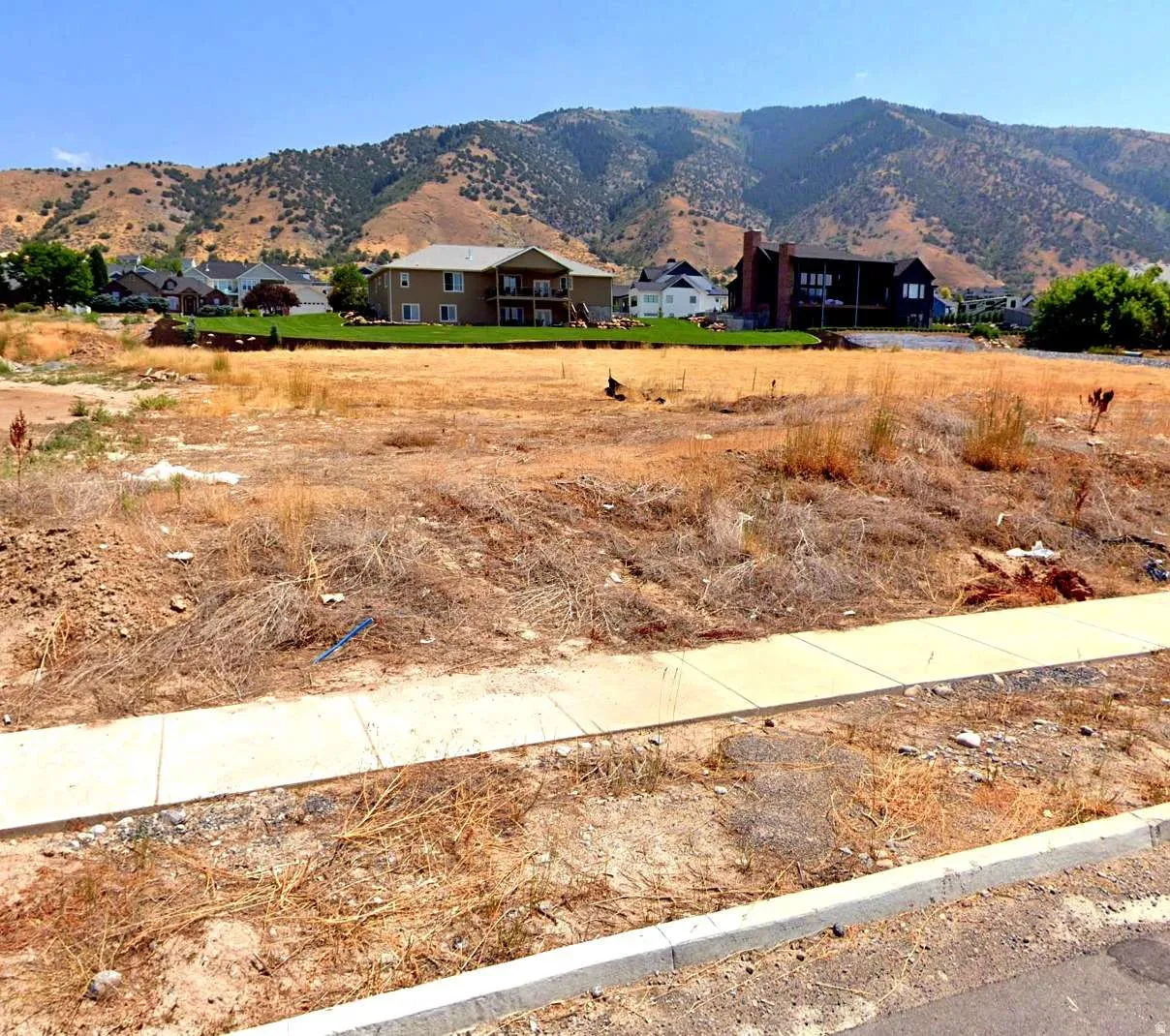 Expansive building lot featuring street frontage, existing curb and sidewalk infrastructure, and mountain scenery