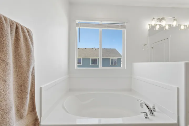 Built-in soaking tub with chrome fixtures, white wall paneling, and a window for natural light