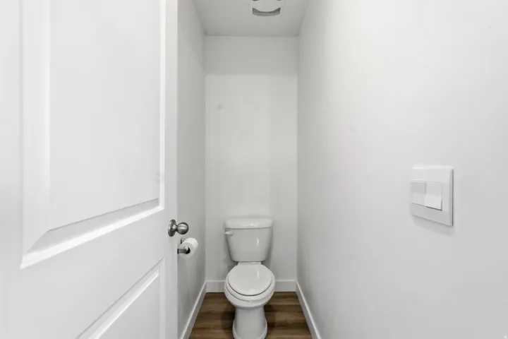 Compact water closet featuring a standard toilet, wood-finish flooring, white baseboards, and a contemporary wall switch