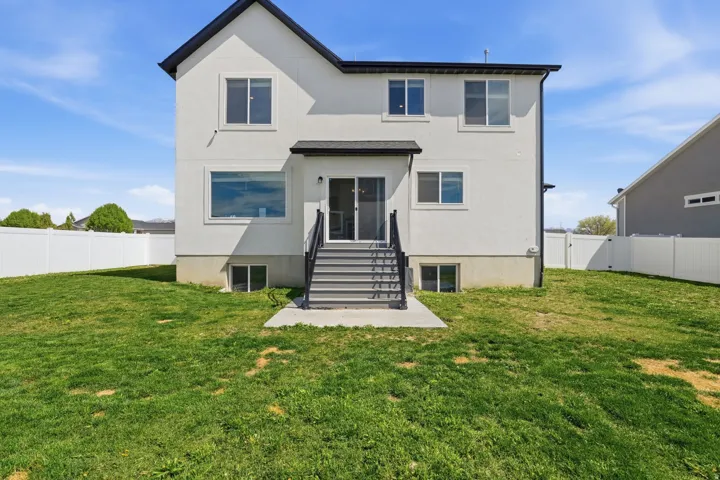 Expansive rear yard featuring a privacy fence, concrete patio, and exterior stairs with dark railings