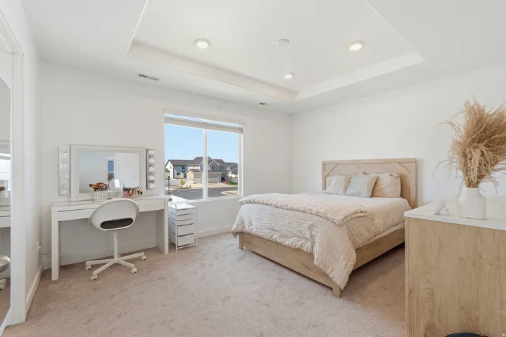 Spacious bedroom featuring light-toned carpeting, a tray ceiling with recessed lighting, and a large window
