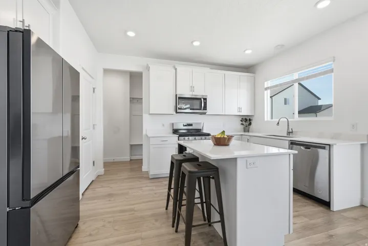 Modern kitchen featuring stainless steel appliances, white cabinetry, a central island with seating, recessed lighting, and wood-finish flooring