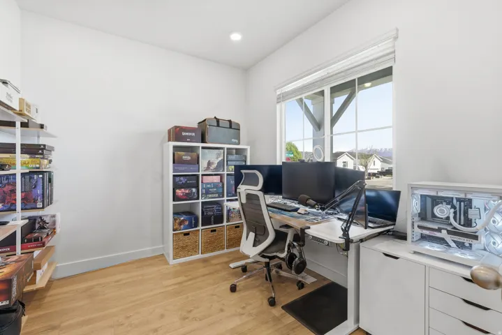 Spacious room featuring light wood-finish flooring, white walls, and a large window with white blinds