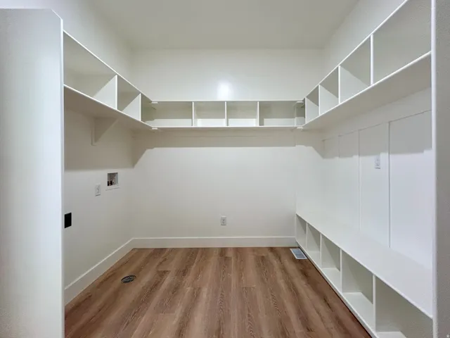 Spacious utility room featuring extensive built-in shelving, wood-finish flooring, and crisp white walls