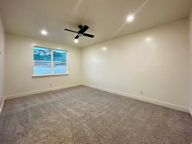 Spacious room featuring neutral carpet, a large window with white trim, recessed lighting, a ceiling fan, and mountain scenery