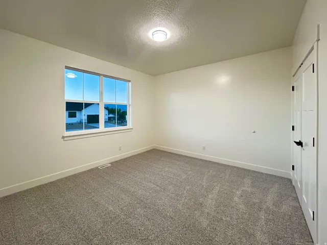Bright room featuring a large window, neutral wall paint, gray carpet, white trim, and a white interior door with black hardware