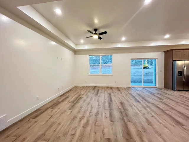Open-concept living space featuring wood-finish flooring, a tray ceiling with recessed lighting, and a ceiling fan