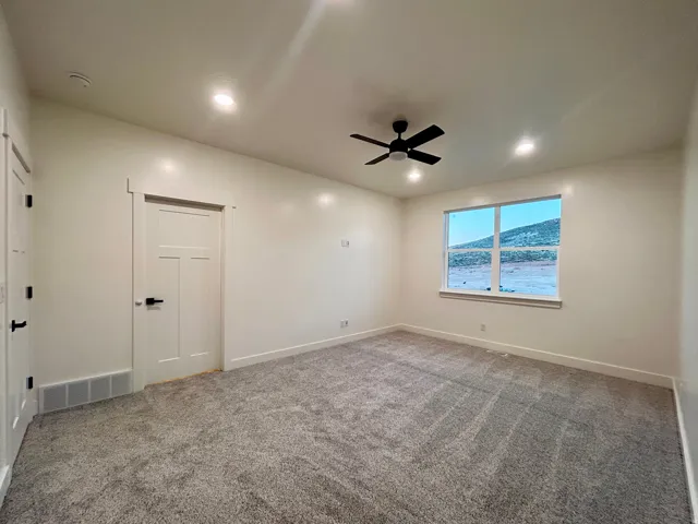 Spacious room featuring neutral carpeting, a large window, a modern black ceiling fan, and recessed lighting