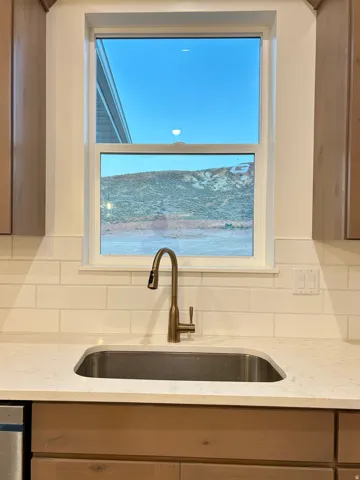 Kitchen sink area featuring a single basin undermount sink, a bronze-finish gooseneck faucet, light-toned countertop, and white subway tile backsplash