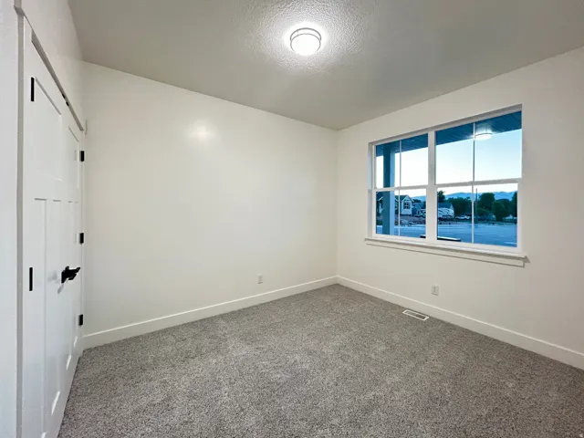 Bright interior space featuring a large window with white trim, gray textured carpet, and white walls