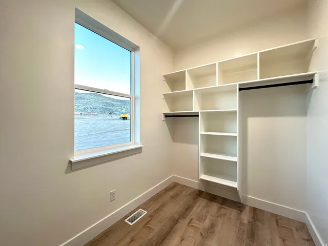 Walk-in closet featuring a window, built-in shelving, two hanging rods, and wood-finish flooring
