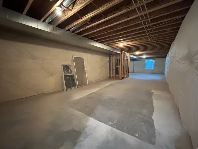 Expansive unfinished lower level featuring exposed ceiling joists, concrete flooring, and an egress window