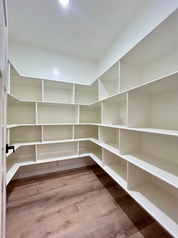 Walk-in pantry featuring extensive built-in shelving, wood-finish flooring, and recessed ceiling lighting