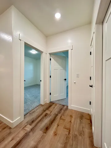 Corridor featuring wood-finish flooring, recessed lighting, white trim, and multiple doorways with modern panel doors