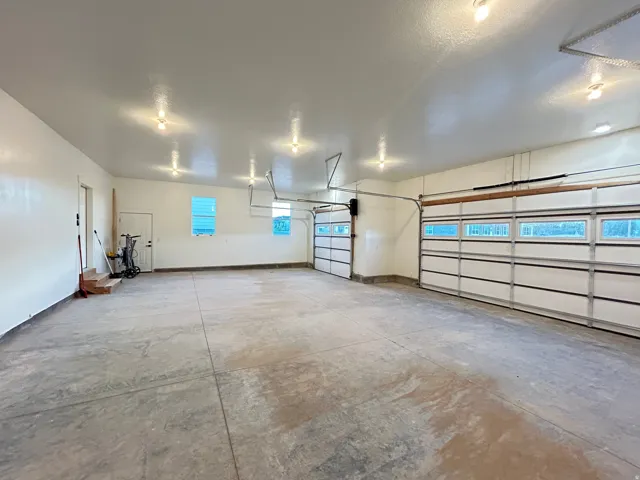 Spacious garage featuring a concrete floor, multiple windows, two overhead doors with frosted glass panels, and bright overhead lighting