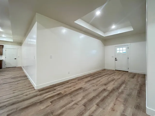 Spacious room featuring wood-finish flooring, white baseboards, and a tray ceiling with recessed lighting