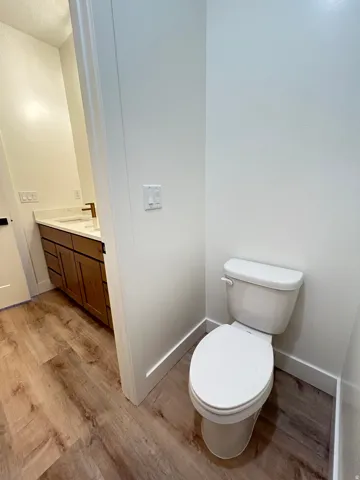 Contemporary powder room featuring a white toilet, wood-finish flooring, and a vanity with a white countertop and dark wood cabinetry