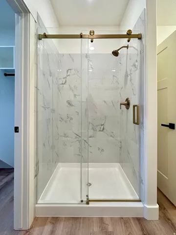 Shower enclosure featuring a sliding glass door, marble-look tile surround, bronze-finish hardware, and a white shower base