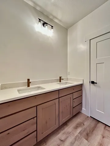 Double vanity with light wood-finish cabinetry, white countertops, and bronze-tone fixtures