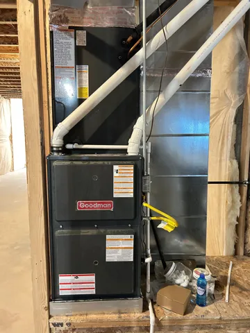 Goodman furnace unit with white PVC piping and exposed wooden framing