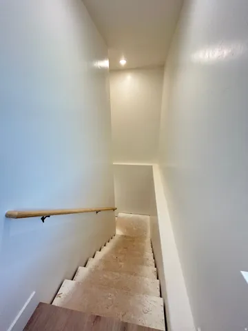 Stairwell with light wood-finish flooring at the landing, a natural wood handrail, recessed lighting, and light-toned walls