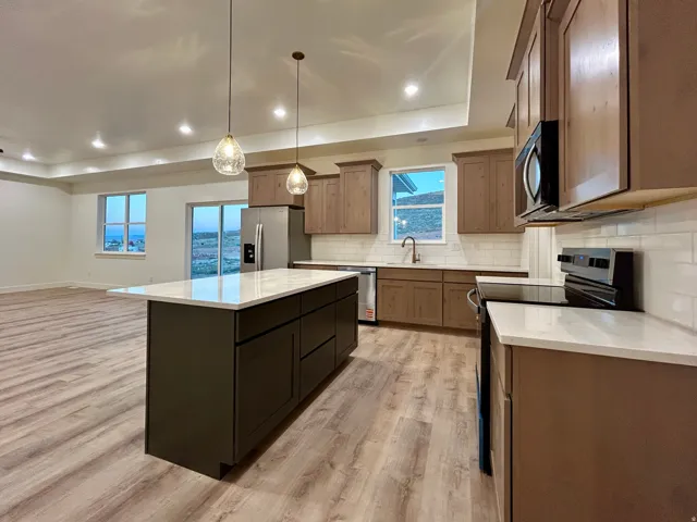 Open-concept kitchen with a central island featuring a white countertop, recessed lighting, and pendulum fixtures
