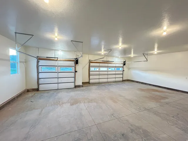 Expansive garage featuring two overhead doors with window inserts, concrete flooring, and multiple ceiling-mounted light fixtures