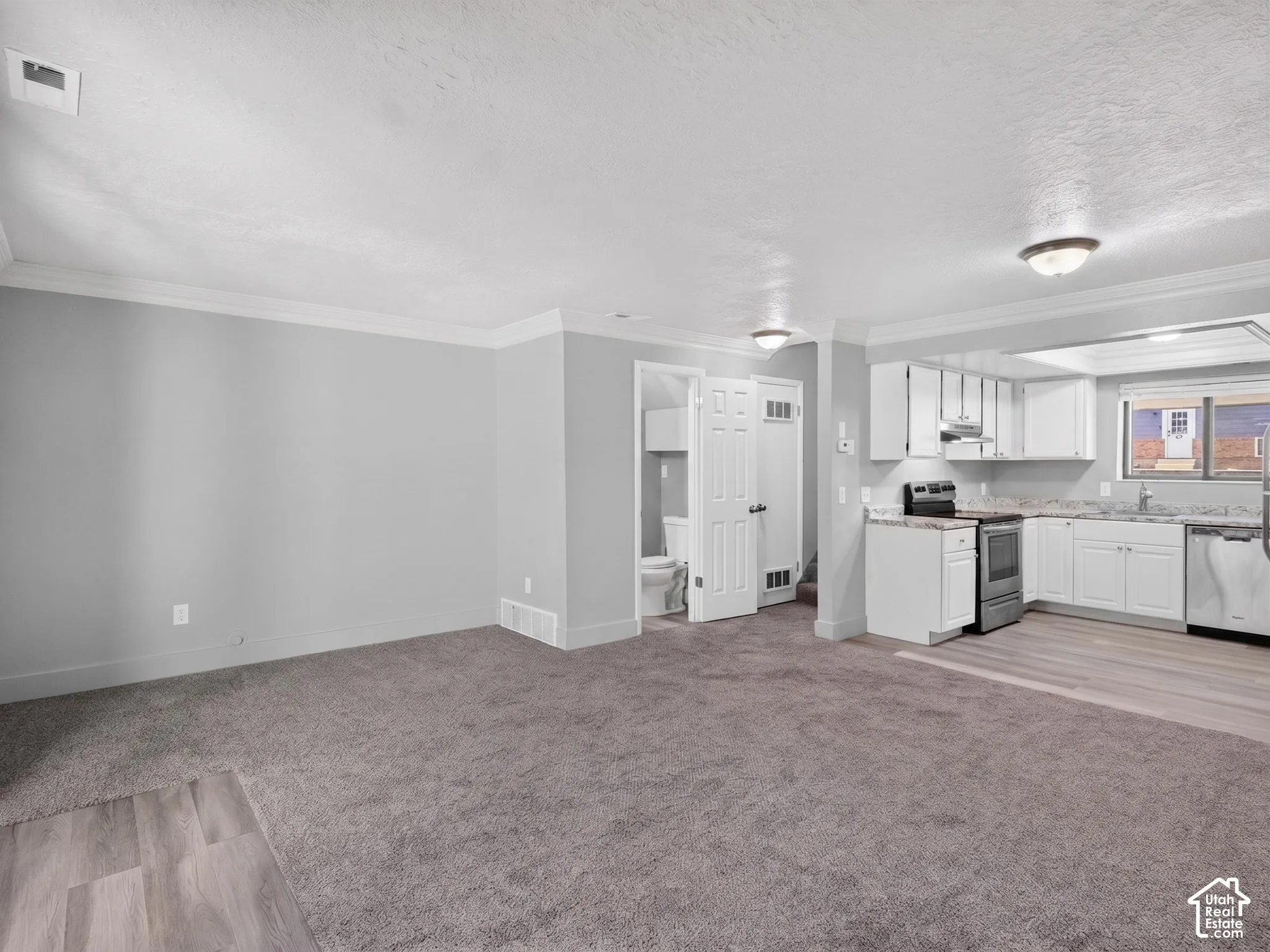 Open-concept living space featuring gray carpeting, light wood-finish flooring, and white crown molding
