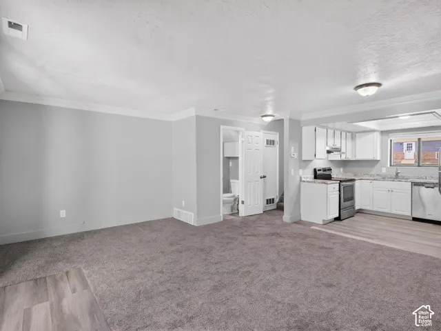 Open-concept living space featuring gray carpeting, light wood-finish flooring, and white crown molding