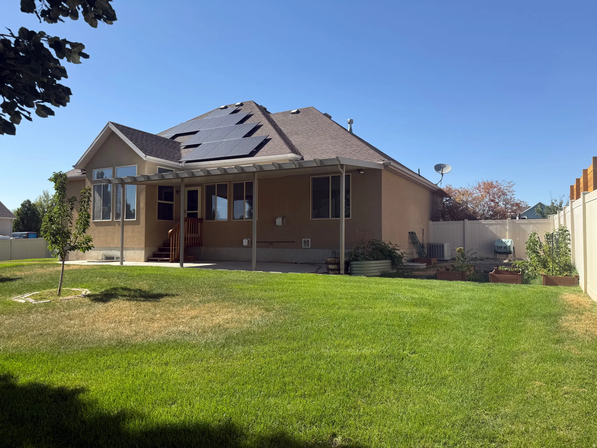 Spacious backyard featuring a large green lawn, a covered patio structure, and multiple raised garden beds