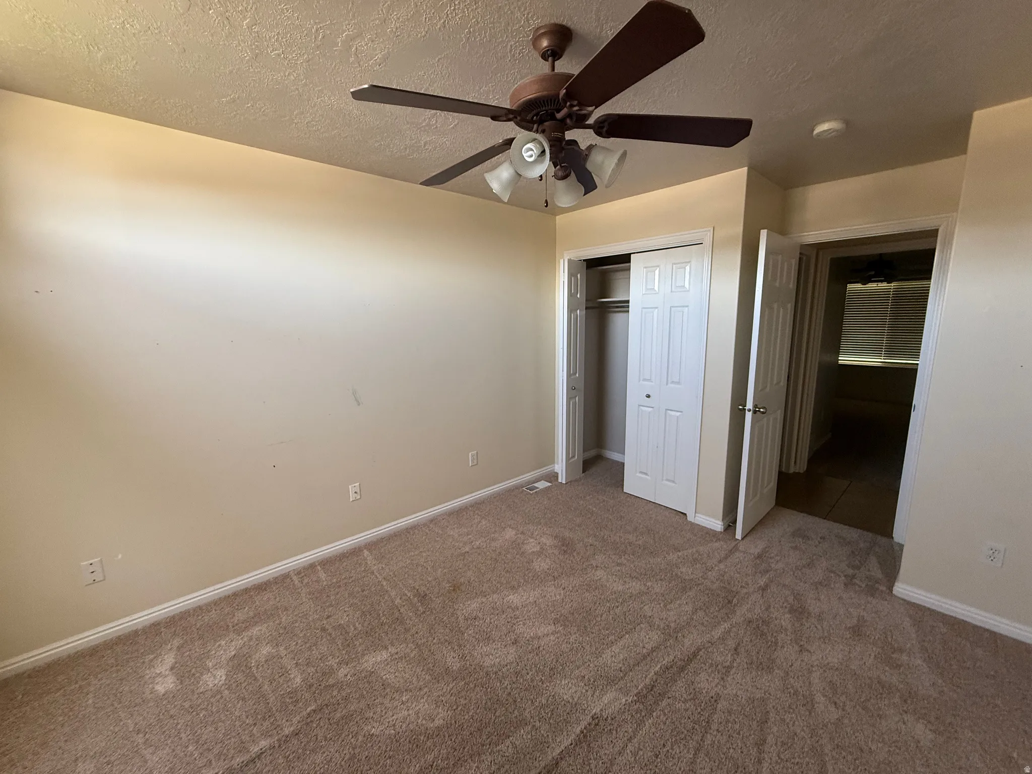 Carpeted interior space featuring a ceiling fan with integrated lighting, a bi-fold door closet, and a doorway opening to another room