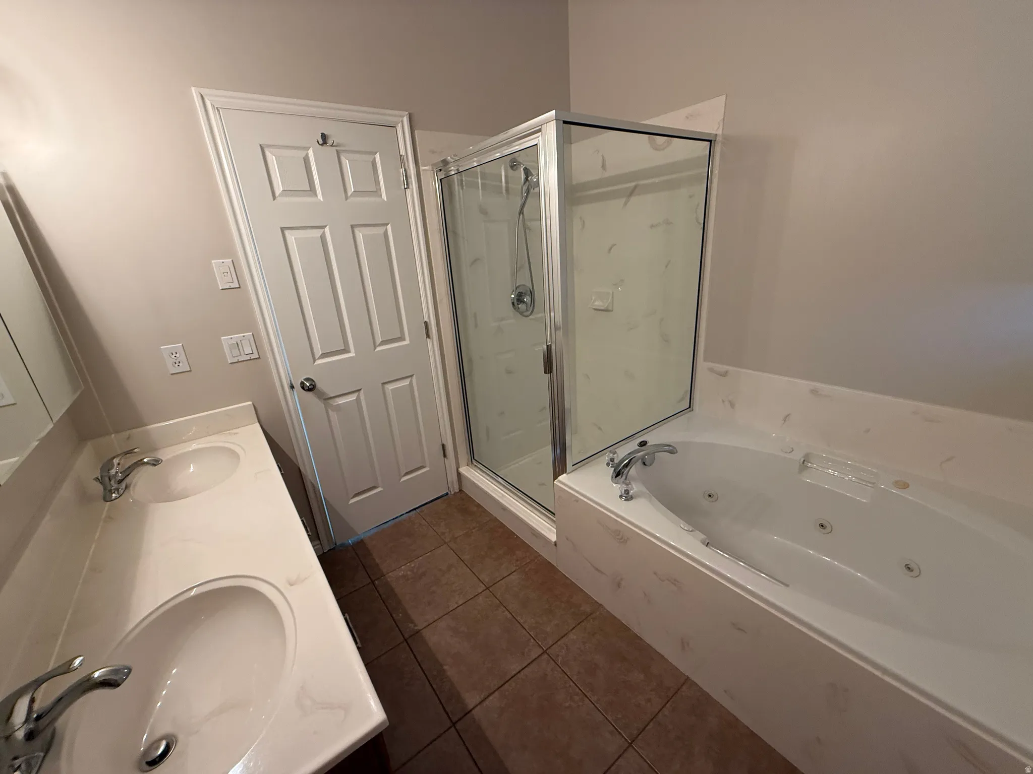 Bathroom featuring a dual vanity with undermount sinks, a built-in jetted tub, a glass-enclosed shower, and brown tile flooring