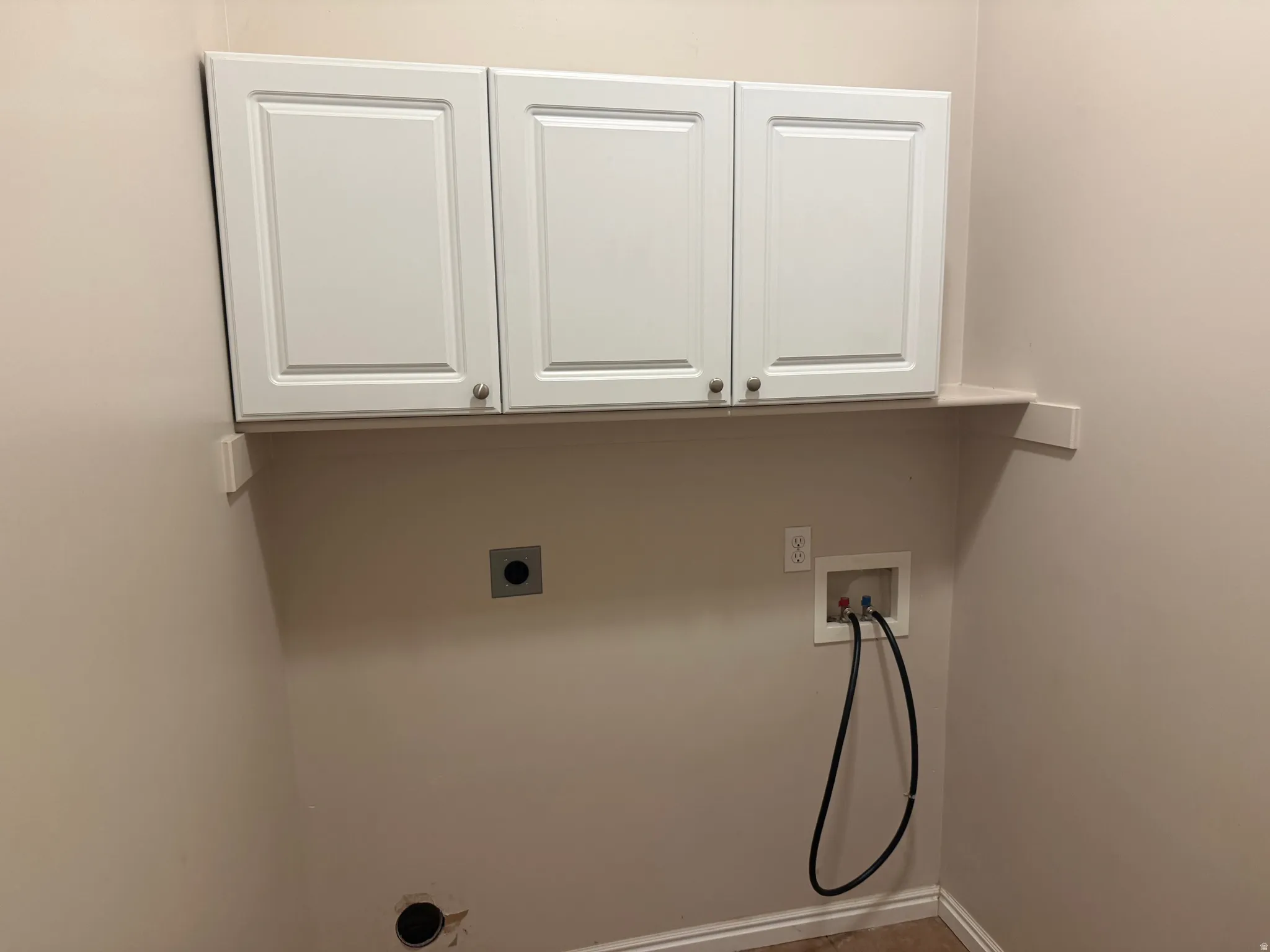 Laundry area featuring three white shaker-style cabinets with brushed nickel hardware, a utility shelf, and laundry hookups