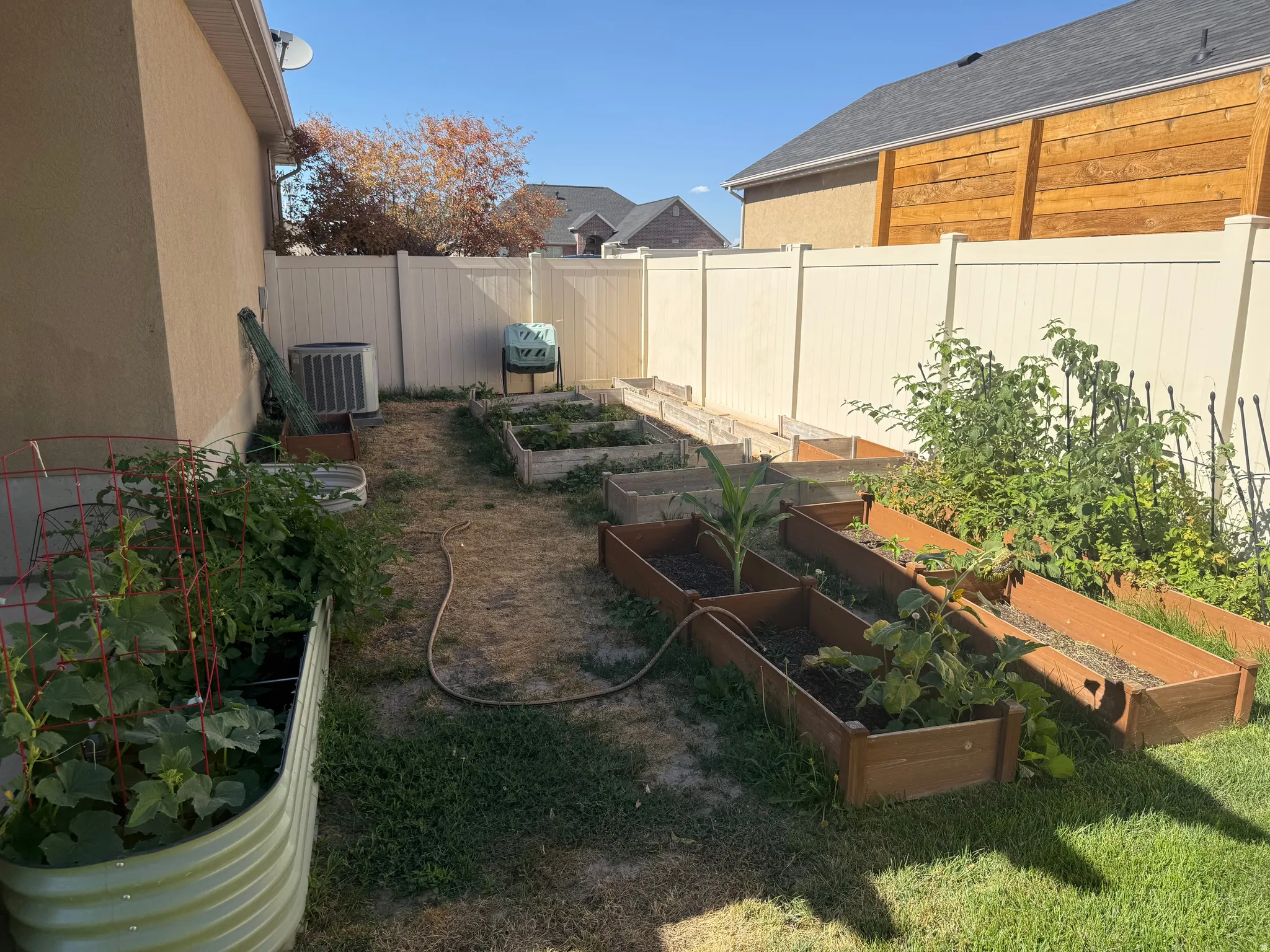 Backyard space featuring multiple raised garden beds, a corrugated metal planter, and an air conditioning unit