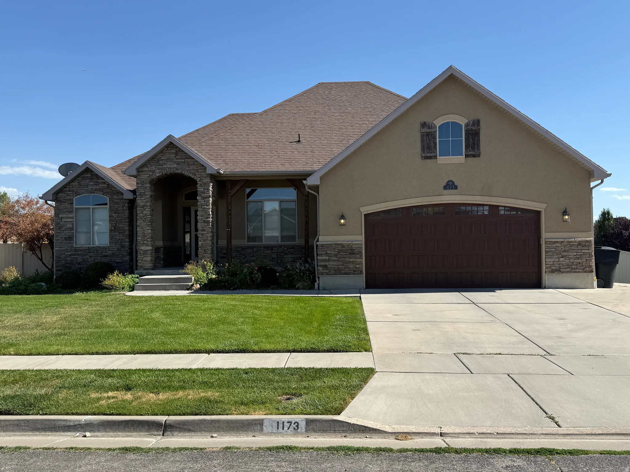 Stucco and stone facade with arched entry, complementing stone accents, and a prominent dark wood-finish garage door