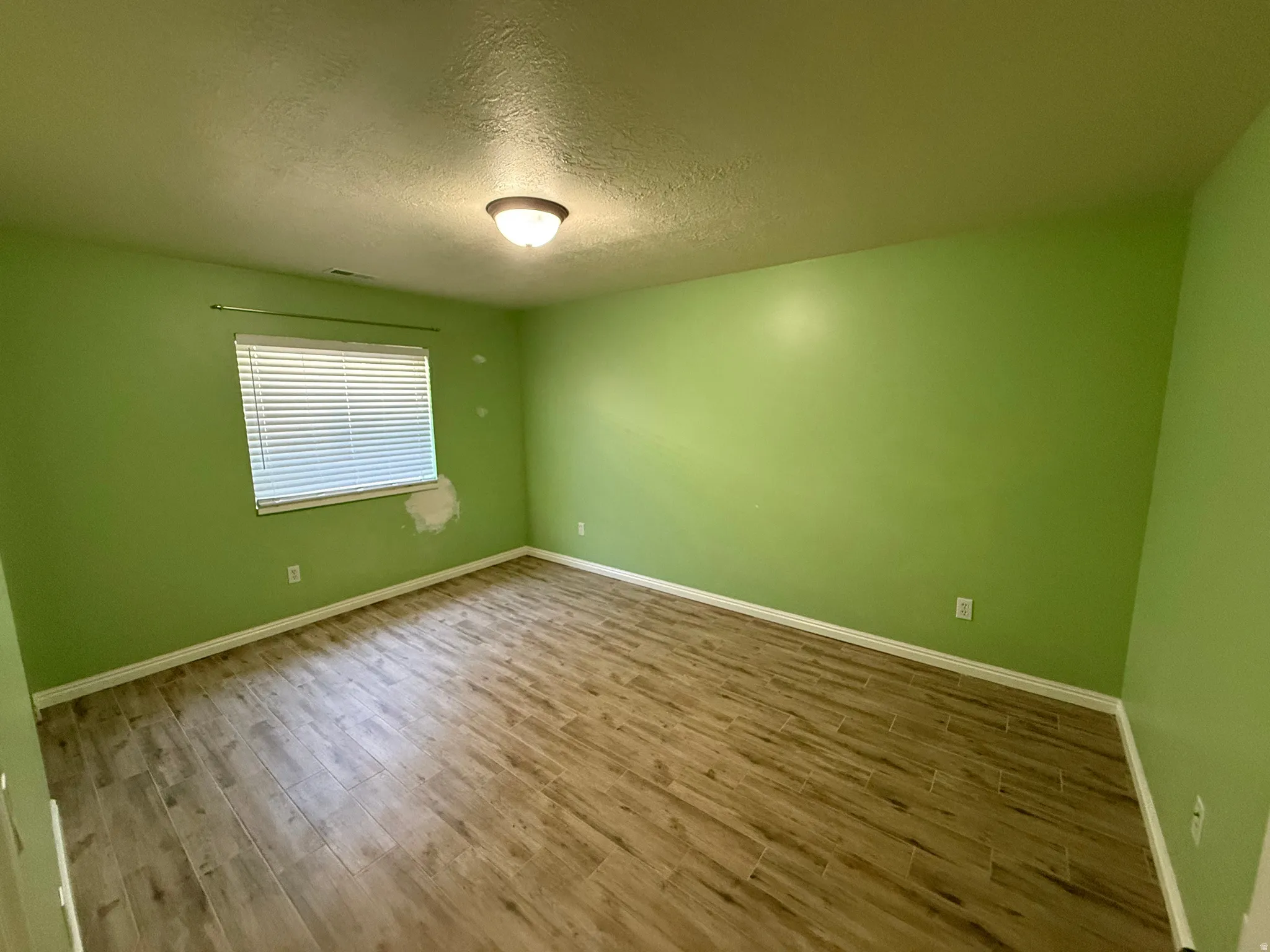 Spacious room featuring wood-finish flooring, a window with blinds, and a ceiling-mounted light fixture