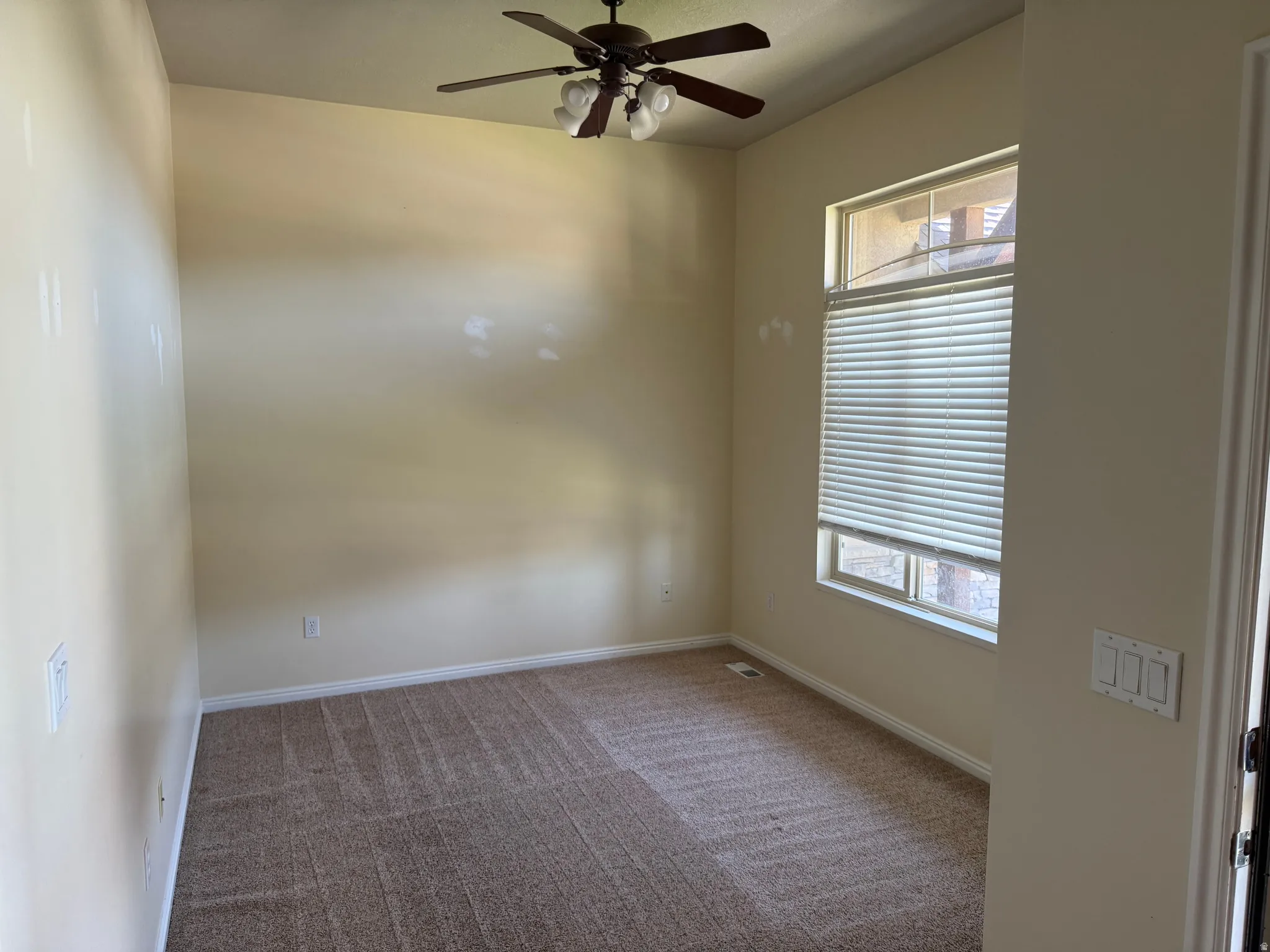 Carpeted room featuring a ceiling fan with integrated lighting, a large window with privacy blinds, and neutral wall tones